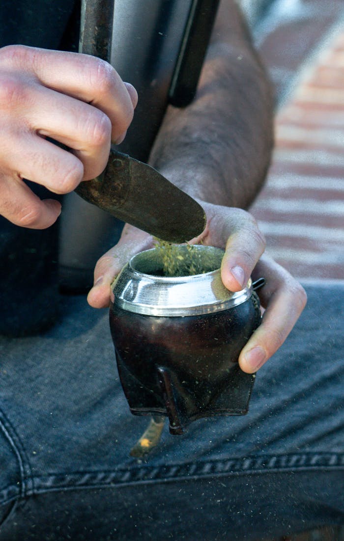 A person scooping yerba mate into a gourd, preparing a traditional South American mate drink.