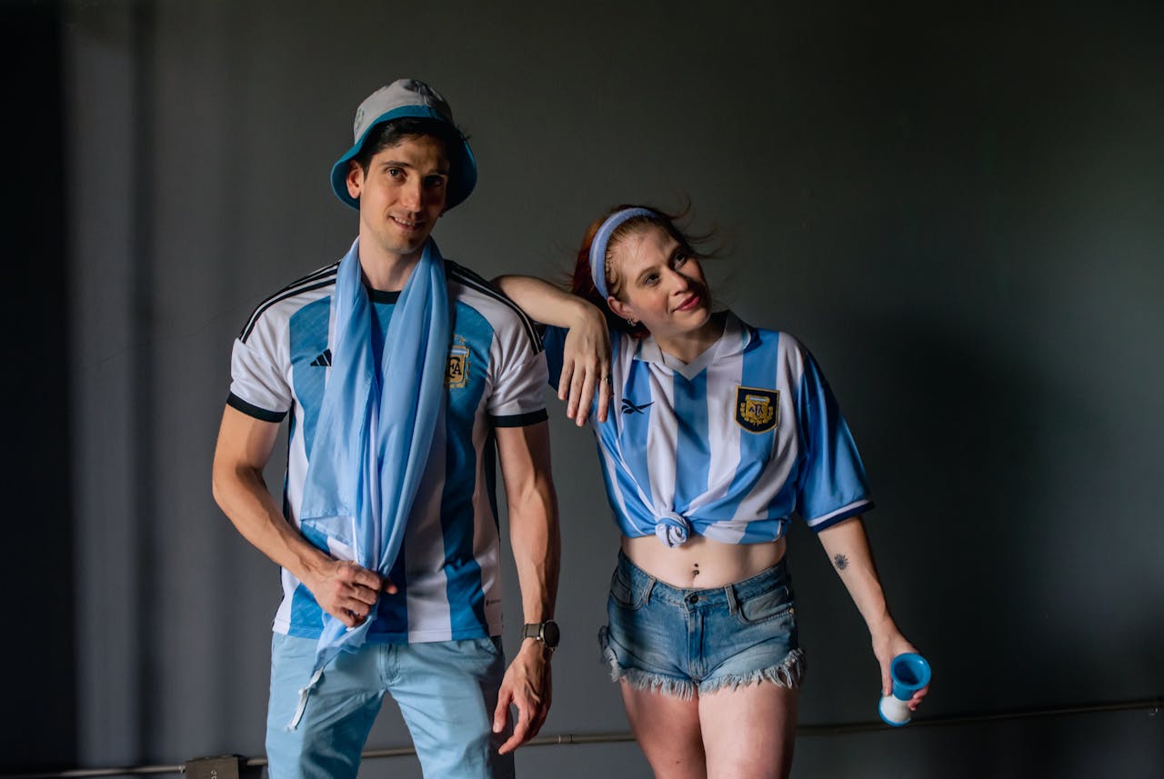 Two adults in Argentina soccer jerseys pose for a casual indoor shot, displaying team spirit.